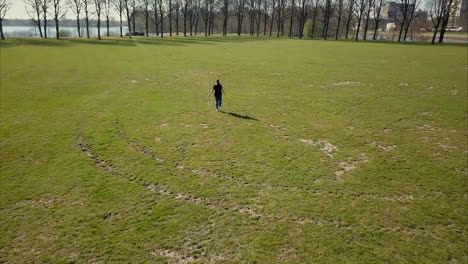 Aerial-drone-shot-of-flying-forward-following-the-adult-woman-in-a-black-t-shirt-walking-in-the-park
