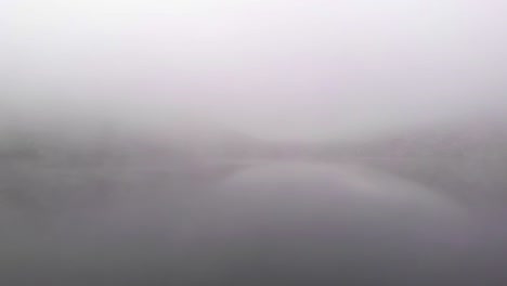 Man-standing-on-a-rock,-foggy-lake-landscape,-drone-shot