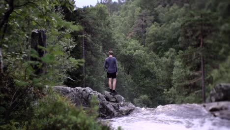Slow-motion-shot-of-a-man-standing-on-rocks-besides-river,-watching-over-beautiful-view-in-Norway,-Europe
