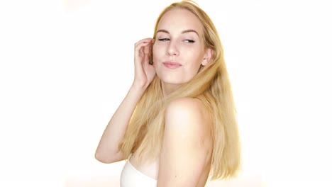 Against-a-plain-white-studio-background,-a-young-woman-with-blonde-hair-looks-over-her-shoulder-and-smiles