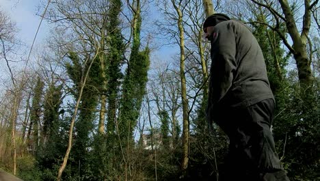 Low-angle-follow-shot-of-male-wearing-hat---scarf-walking-in-bare-woodland-trees-on-cold-sunny-day