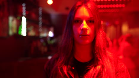 Young-caucasian-female-with-long-hair-walking-towards-the-camera,-in-a-bar-with-red-lighting
