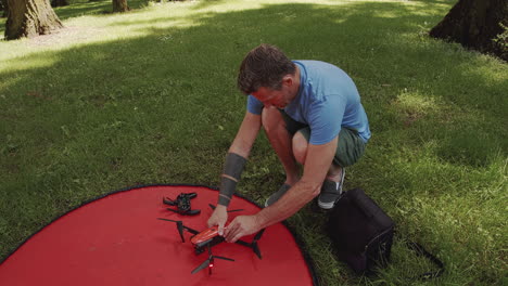 Man-packs-up-small-drone-after-flight-in-park,-sunny-day,-close-up