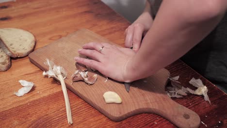Woman's-hands-with-a-knife-crush-the-garlic-on-a-chopping-board,-then-peel-the-skin-1