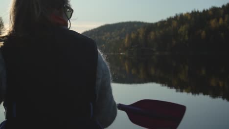 Woman-paddling-canoe-on-beautiful-lake-in-autumn,-rear-view-closeup-slow-motion
