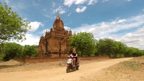 Girl-Rides-Motorbike-on-Quiet-Road-In-Front-of-a-Large-Temple