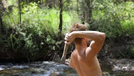 Slow-motion-shot-of-a-shirtless-man-practicing-his-axe-throwing-skill-by-trying-to-throw-his-hatchet-at-a-pine-tree-4