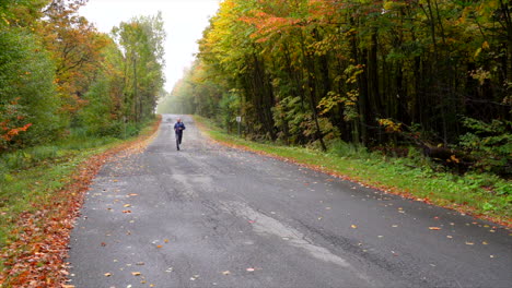 Man-running-on-a-small-road-surrounded-by-maple-autumn-maple-leaf-slowmotion