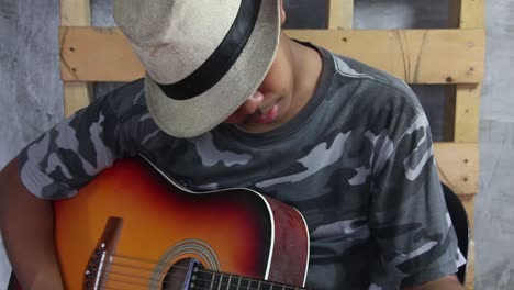 Asian-male-teen-wearing-fedora-tuning-a-classical-guitar