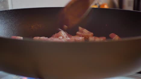 Close-up-shallow-focus-on-fresh-chopped-bacon-pieces-in-hot-steaming-frying-pan-on-cooker-stove
