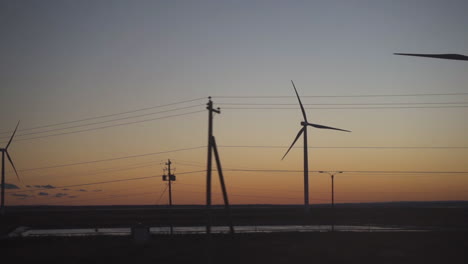 Pan-right-to-left-clean-green-energy-wind-turbines-at-sunset-in-field