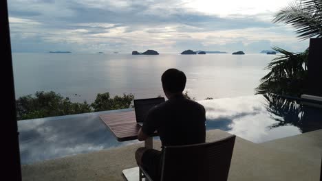 Asian-man-working-on-the-laptop-by-the-pool---back-view-1