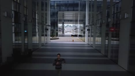Aerial-shot-of-a-young-male-in-casual-clothes-as-he-runs-through-a-deserted-futuristic-office-street
