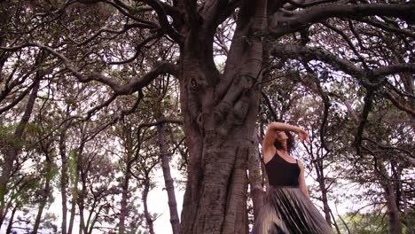Hermosa-Mujer-Bailando-Con-Gracia-Bajo-El-Enorme-árbol-En-El-Bosque-De-Pinos-En-Australia---Tiro-De-ángulo-Bajo