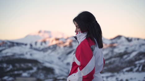 Eine-Schöne-Frau-In-Winterkleidung-Beobachtet-Den-Sonnenuntergang-über-Einer-Gruppe-Schneebedeckter-Berge-In-Der-Abenddämmerung