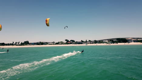 Beautiful-pickup-shot-of-kite-surfers-in-full-sails-approaching-Langebaan-Beach,-South-Africa-on-a-bright-sunny-day