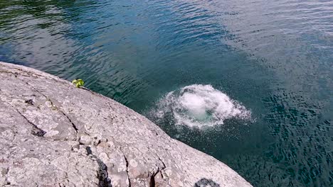 Young-White-Man-Jumps-Off-Rock-Cliff-Into-Blue-Lake-in-Slow-Motion,-Wide-Pan-Overhead