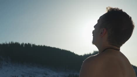 Close-up-view-behind-man-breathing-heavily-while-sitting-outside-in-cold-mountain-environment-with-no-shirt
