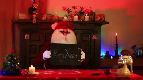 Santa-Claus-Mostrando-Nota-De-Feliz-Navidad-En-Pizarra-Negra