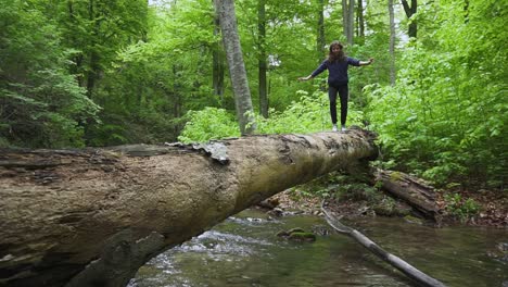 A-girl-balances-on-a-log-bridge-as-she-crosses-a-small-stream-while-hiking