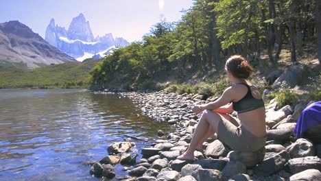 Young-woman-sitting-beside-the-lake-in-Laguna-Carpi,-looking-at-the-Fitz-Roy-in-Patagonia,-Argentina