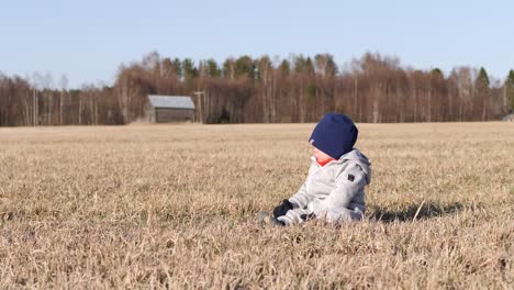 Toddler-boy-sitting-alone-in-rural-field,-springtime