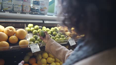 At-the-grocery:-Attractive-young-African-American-woman-taking-choosing-lime-with-bag-buying-limes-at-fruit-vegetable-supermarket-marketplace
