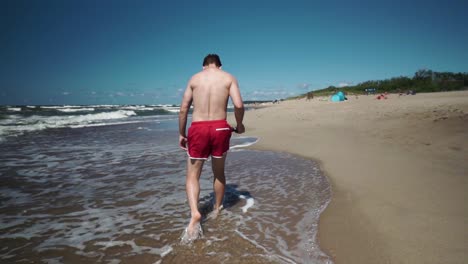 Young-man-in-red-shorts-walks-in-a-beach-by-the-sea-1
