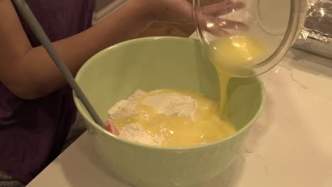 A-girl-pours-melted-butter-into-a-large-bowl-with-flour-and-sugar-inside