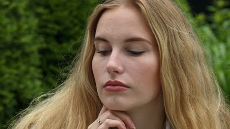 Static-close-up-shot-of-a-blonde-model's-face-while-resting-her-chin-on-her-hand-thinking