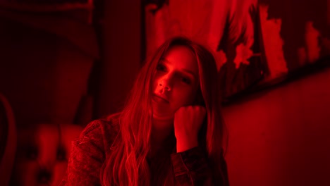 Female-with-long-hair-sitting-in-a-bar-with-red-neon-lighting-looking-at-the-camera