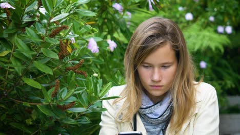 Attractive-teenage-girl-checks-social-media-messages-on-her-smartphone-sitting-in-the-garden