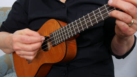 Close-up-view-of-woman-playing-a-ukulele,-no-face,-plucking-strings,-Handheld