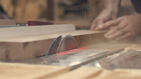 A-piece-of-wood-is-cut-on-a-buzz-saw-by-a-carpenter,-slow-motion-low-angle-close-up