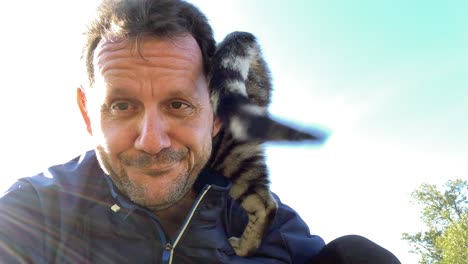Lovely-cat-climbing-on-shoulder-of-adult-man-outdoor-on-sunny-day,close-up