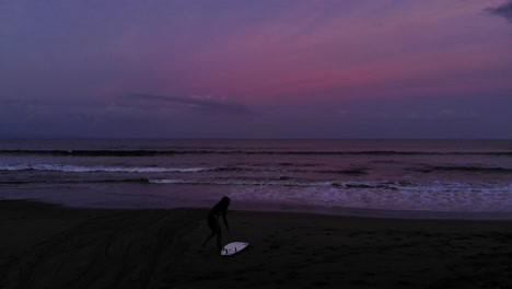 Silhouette-Female-Surfer-Getting-Ready-On-The-Beach-At-Sunrise-Aerial-Flyover