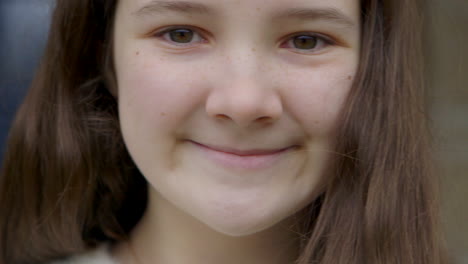Close-up-of-sweet-teenage-girl-with-brown-eyes-smiling-at-camera,-hand-held-camera