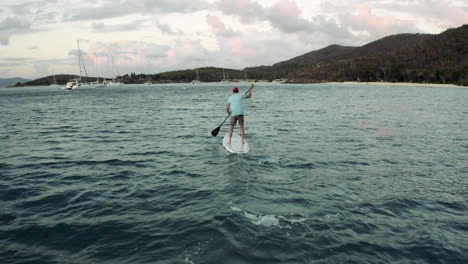 Drone-follows-as-stand-up-paddle-boarder-rows-toward-a-hilly-island-in-the-Caribbean