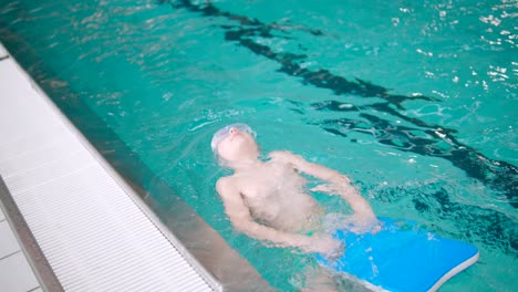 El-Niño-Está-Practicando-Nadar-Hacia-Atrás-Dentro-De-Una-Gran-Piscina-Con-Tabla-De-Natación