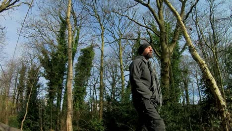Low-angle-follow-shot-of-male-in-hat---scarf-walking-through-sunny-cold-woodland-trees
