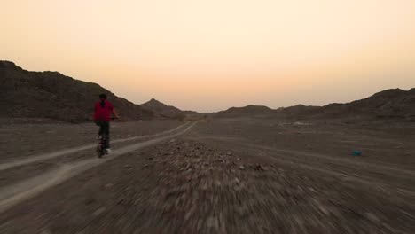 Young-teenager-riding-a-folding-bike-in-a-flat-off-road-terrain-by-the-mountains-in-Fujairah,-United-Arab-Emirates