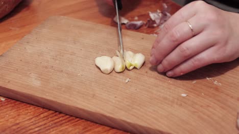 Woman's-hands-with-a-knife-chops-the-first-clove-of-garlic-on-a-chopping-board