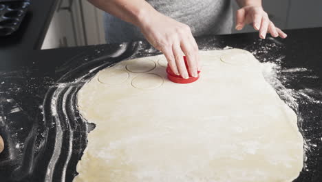 Dough-rolled-out-on-a-black-counter-and-woman-using-a-mold-to-cut-shapes-into-dough-for-baking