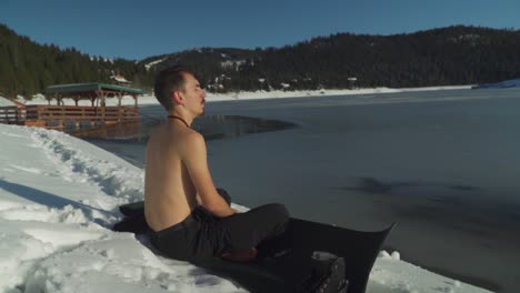 Man-sitting-on-yoga-mat-beside-frozen-lake