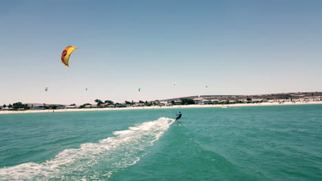 Ultra-wide-drone-shot-chasing-a-kite-surfer-on-full-speed-in-beautiful-natural-daylight-sun-with-blue-sky-on-Langebaan-Beach,-Cape-Town,-South-africa-with-summer-vacation-beachscape