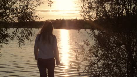 Woman-silhouette-walking-towards-rippling-lake-at-sunset