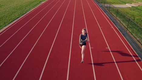 Teen-girl-athlete-sprints-on-a-high-school-track-aerial-camera-preceding