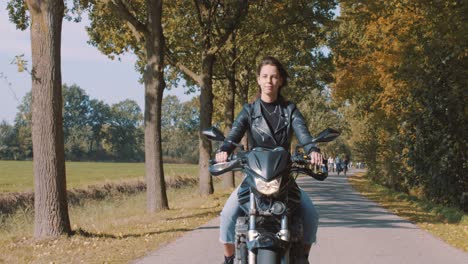 Pretty-smiling-European-young-woman-driving-a-motorbike-wearing-leather-jacket-in-forest-with-vibrant,-colorful-golden-autumn-leaves-on-sunny-day-8