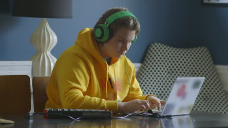 Teenage-boy-wearing-headphones-and-working-on-a-laptop-with-a-midi-controller,-medium-profile