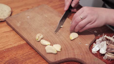 Woman's-hands-with-a-knife-crush-the-last-clove-of-garlic-on-a-chopping-board,-then-peel-the-skin
